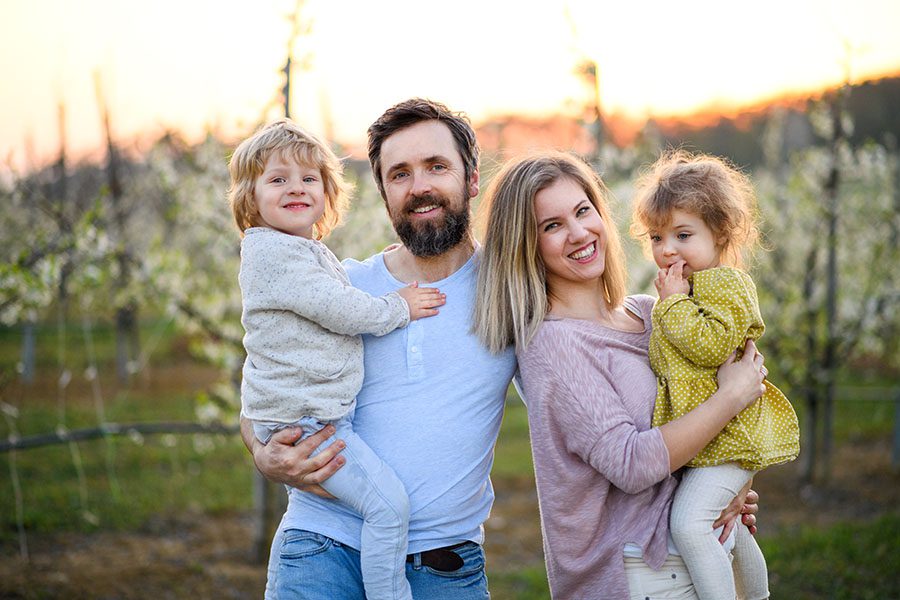 Personal Insurance - Portrait of Happy Family with Young Kids Standing Outside in an Orchard